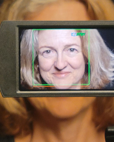 Photograph of author Kay DiMarco's face within a video camera viewfinder
