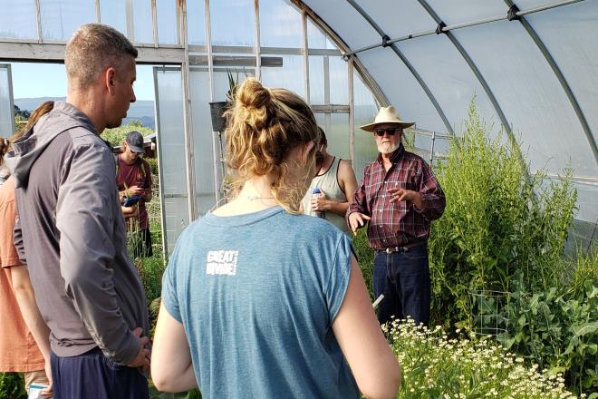 students in a greenhouse listening to a farmer talk
