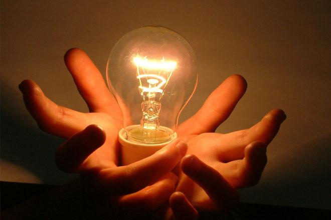 Photograph of an illuminated lightbulb held within a person's palms